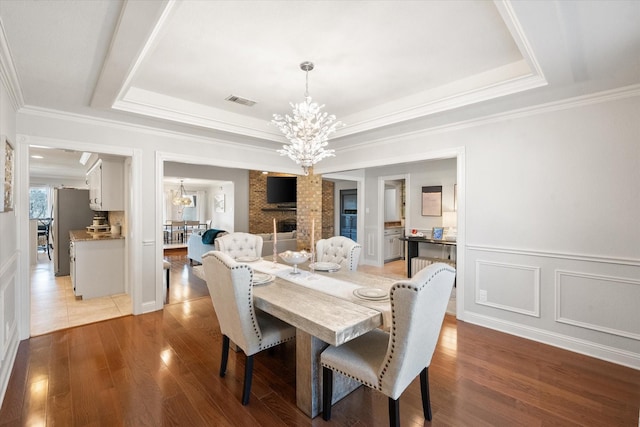 dining space with a chandelier, a raised ceiling, visible vents, and wood finished floors