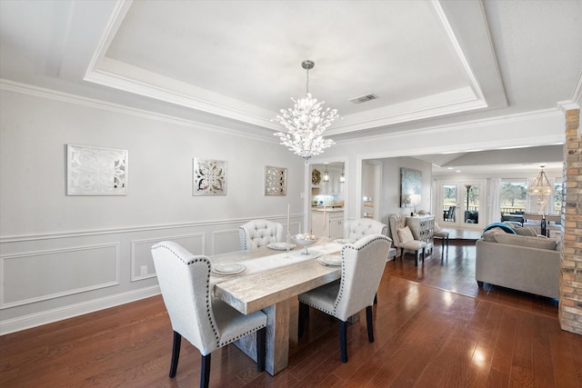 dining area with dark wood-style floors, a notable chandelier, visible vents, and a tray ceiling