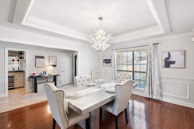 dining area featuring a wainscoted wall, a raised ceiling, ornamental molding, wood finished floors, and beverage cooler