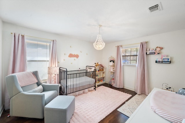 bedroom featuring an inviting chandelier, wood finished floors, visible vents, and baseboards