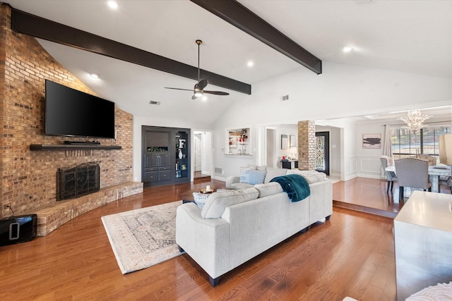 living room with a brick fireplace, a decorative wall, wood finished floors, and beamed ceiling