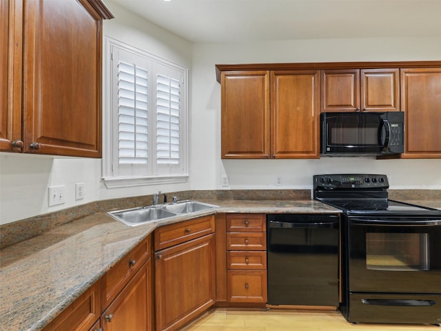 kitchen with brown cabinets, light wood-style flooring, a sink, dark stone counters, and black appliances