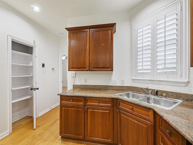 kitchen featuring recessed lighting, a sink, baseboards, light wood-type flooring, and brown cabinets