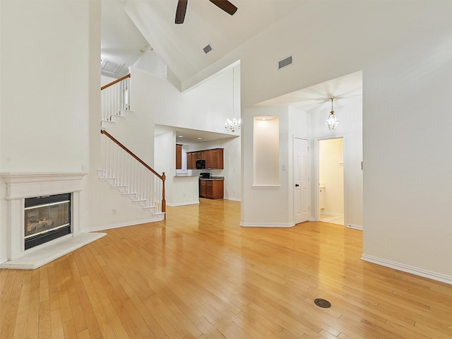 unfurnished living room with light wood-style flooring, visible vents, baseboards, stairway, and a glass covered fireplace