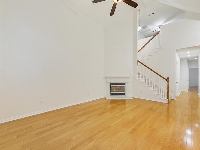 unfurnished living room featuring a towering ceiling, baseboards, stairs, light wood-type flooring, and a glass covered fireplace