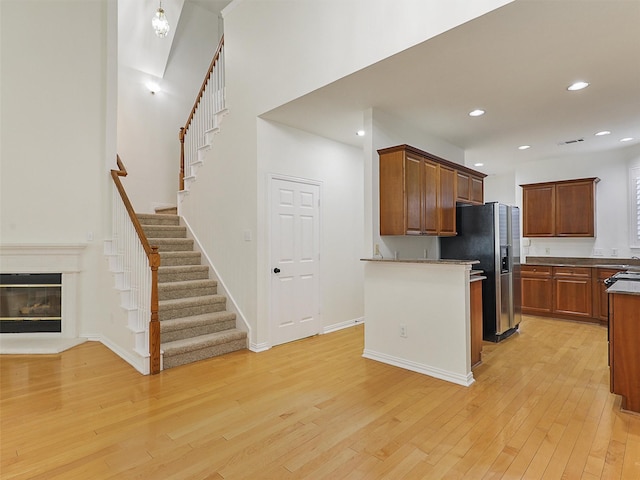 kitchen with recessed lighting, baseboards, light wood-style floors, stainless steel refrigerator with ice dispenser, and a glass covered fireplace