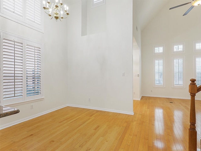 unfurnished room with ceiling fan with notable chandelier, high vaulted ceiling, light wood-style flooring, and baseboards