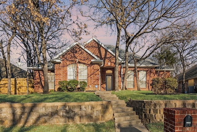 view of front facade with a yard, brick siding, fence, and central AC