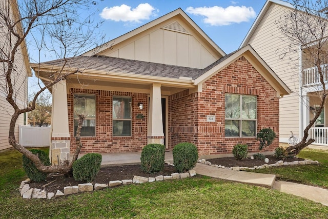 view of front of property featuring a porch, board and batten siding, a front yard, a shingled roof, and brick siding