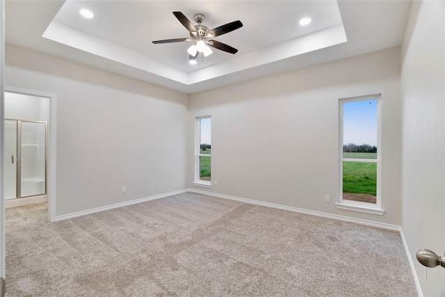 unfurnished room featuring carpet floors, baseboards, a tray ceiling, and a ceiling fan