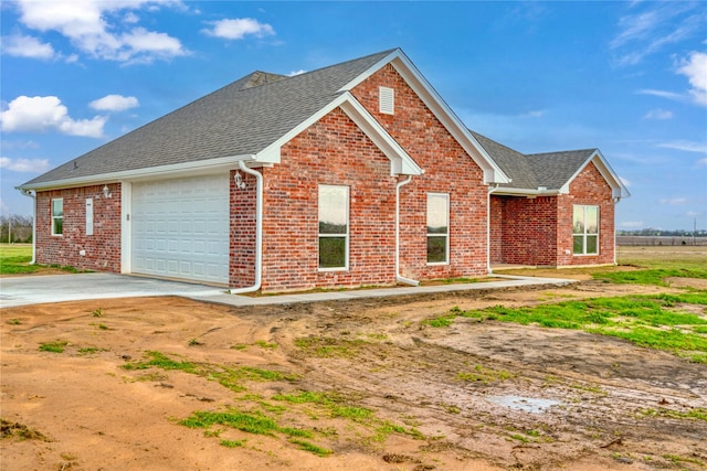 view of front facade with a shingled roof, brick siding, driveway, and an attached garage