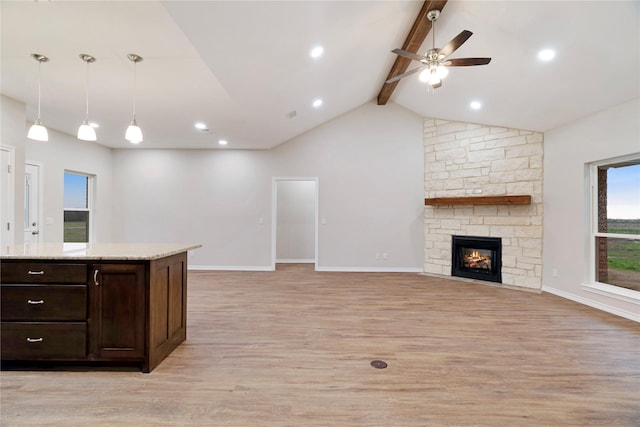 kitchen with vaulted ceiling with beams, light wood-style flooring, open floor plan, a stone fireplace, and dark brown cabinets