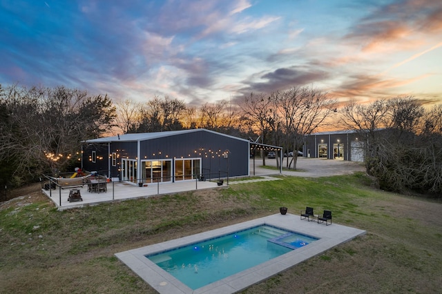 back of house at dusk with a yard, a patio, and an outdoor pool