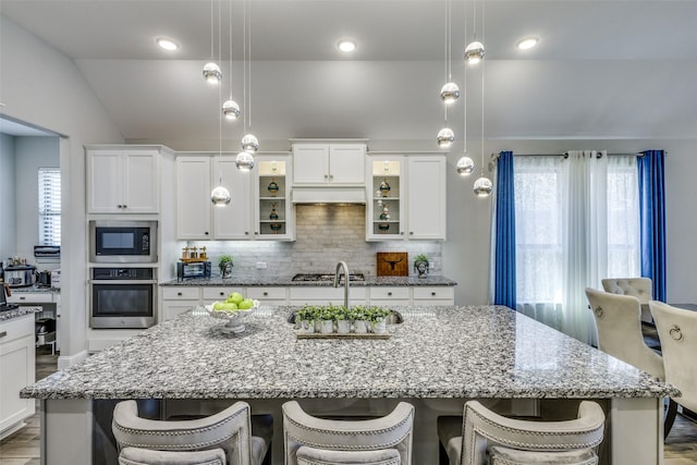 kitchen featuring decorative backsplash, an island with sink, a breakfast bar area, built in microwave, and stainless steel oven