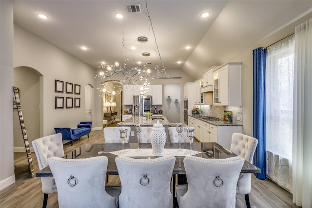 dining space with arched walkways, recessed lighting, visible vents, light wood-style floors, and vaulted ceiling