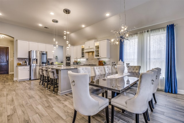 dining space featuring arched walkways, lofted ceiling, visible vents, baseboards, and light wood finished floors