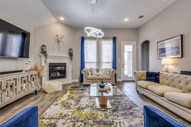 living room featuring baseboards, vaulted ceiling, wood finished floors, and a glass covered fireplace