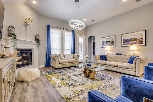 living room featuring arched walkways, a chandelier, recessed lighting, wood finished floors, and a glass covered fireplace