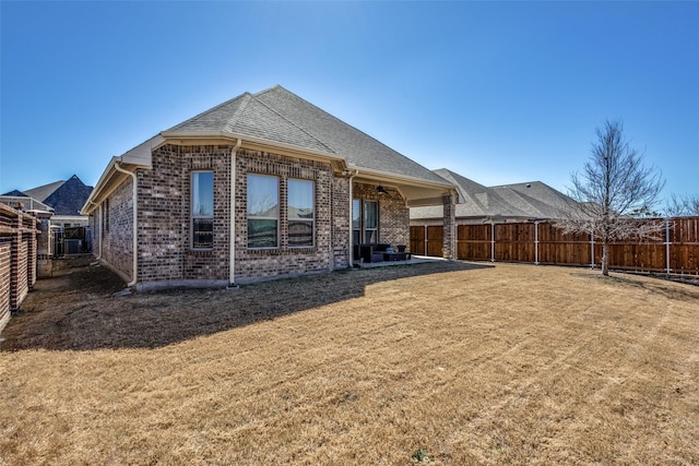 back of house with a fenced backyard, brick siding, a shingled roof, a lawn, and a patio area