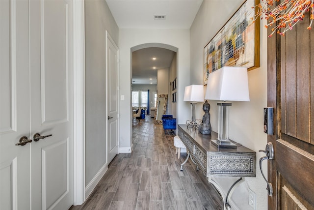 hallway with arched walkways, wood finished floors, visible vents, and baseboards