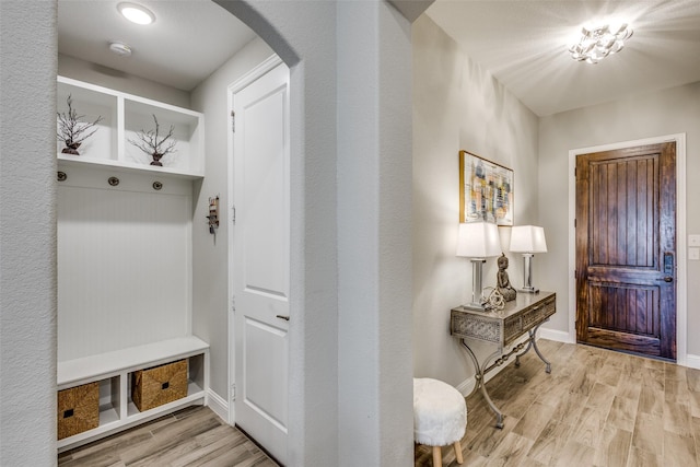 mudroom featuring baseboards, arched walkways, and light wood-style floors