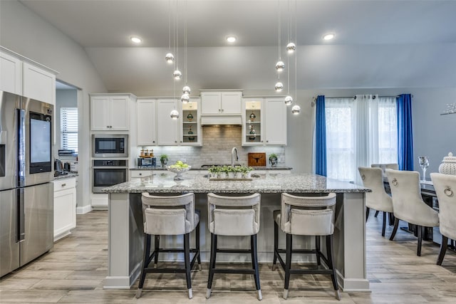 kitchen with a center island with sink, stainless steel appliances, lofted ceiling, backsplash, and light stone countertops