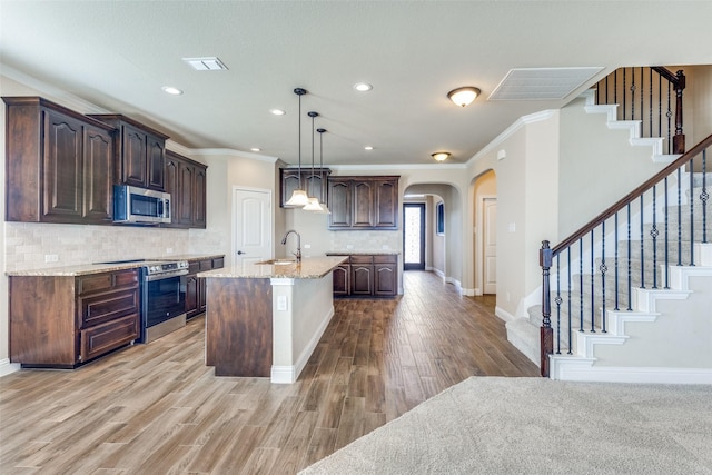 kitchen with arched walkways, dark brown cabinets, appliances with stainless steel finishes, and a sink