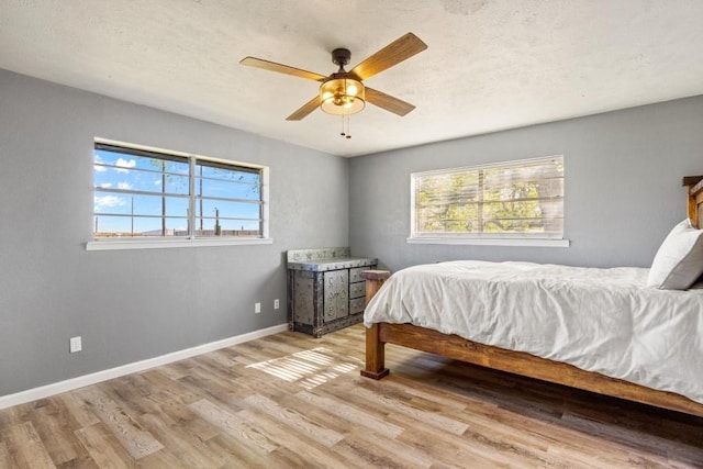 bedroom featuring light wood-style flooring, baseboards, a textured ceiling, and a ceiling fan