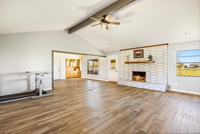 unfurnished living room featuring a brick fireplace, a ceiling fan, wood finished floors, and lofted ceiling with beams
