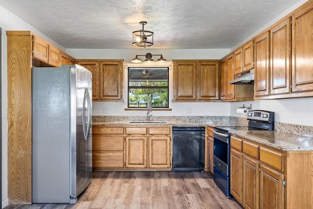 kitchen featuring under cabinet range hood, brown cabinetry, appliances with stainless steel finishes, a sink, and wood finished floors