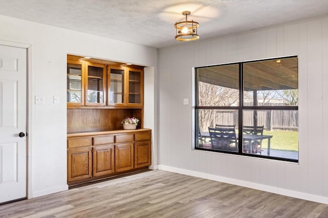 unfurnished dining area with light wood-style floors, baseboards, and a textured ceiling