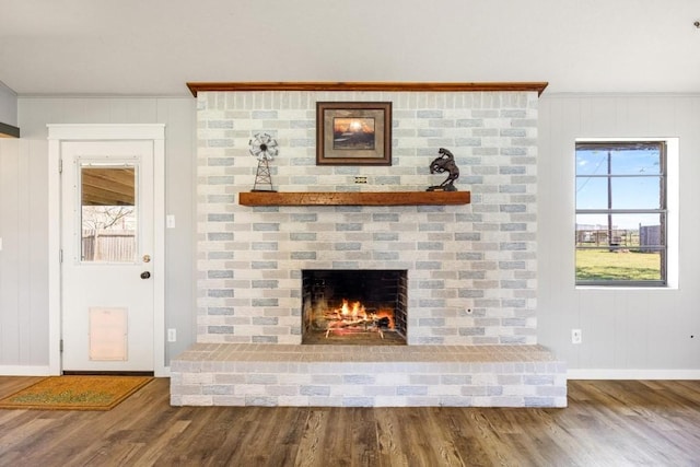 unfurnished living room featuring crown molding, wood finished floors, baseboards, and a brick fireplace