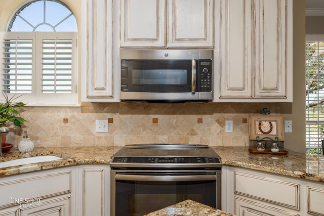 kitchen with a sink, cream cabinetry, electric range oven, tasteful backsplash, and stainless steel microwave