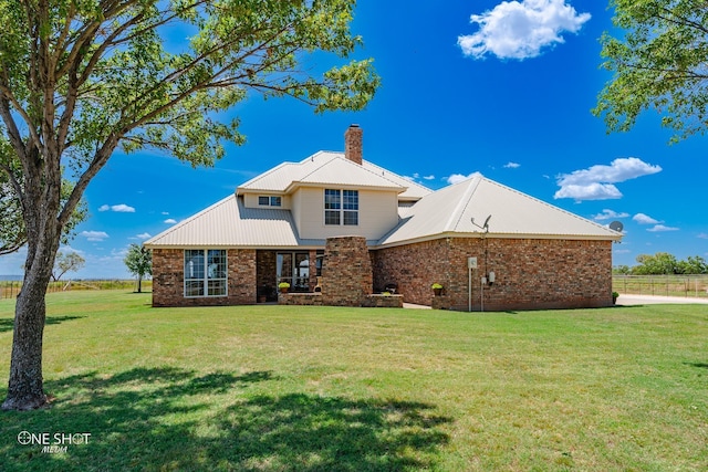 back of house featuring metal roof, a yard, brick siding, and a chimney