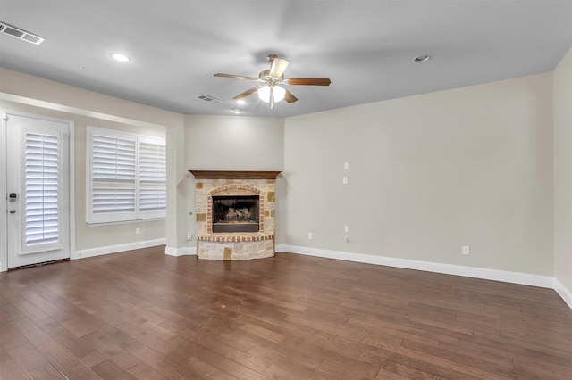 unfurnished living room featuring a ceiling fan, visible vents, dark wood-type flooring, and a stone fireplace