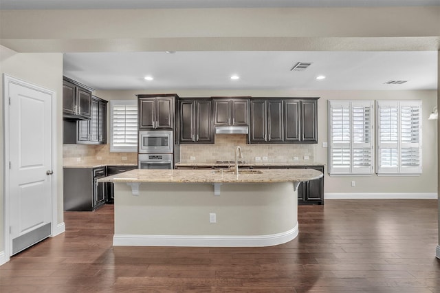 kitchen with light stone counters, dark wood-style flooring, stainless steel appliances, and a sink