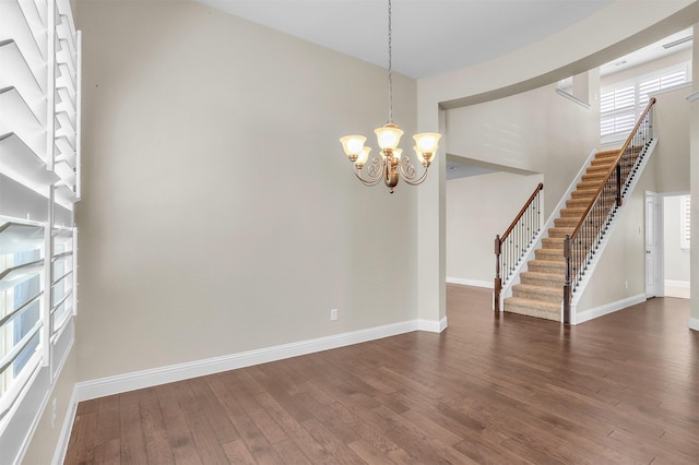 unfurnished room with a high ceiling, baseboards, stairway, dark wood finished floors, and an inviting chandelier