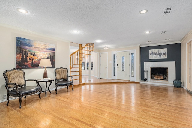 living area with visible vents, ornamental molding, wood finished floors, a tile fireplace, and stairs