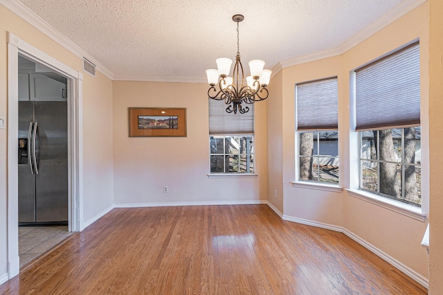 unfurnished dining area featuring an inviting chandelier, crown molding, visible vents, and wood finished floors