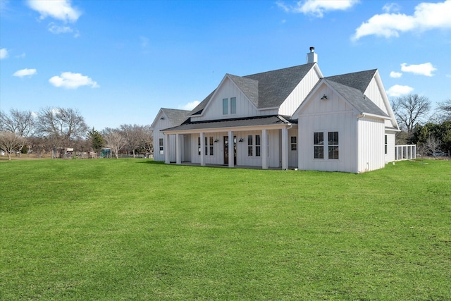 rear view of house featuring a lawn, board and batten siding, a chimney, and roof with shingles