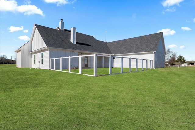 rear view of house featuring a lawn, board and batten siding, a chimney, and a shingled roof