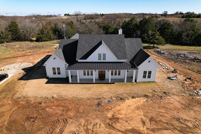 rear view of house with metal roof, board and batten siding, a chimney, and a standing seam roof