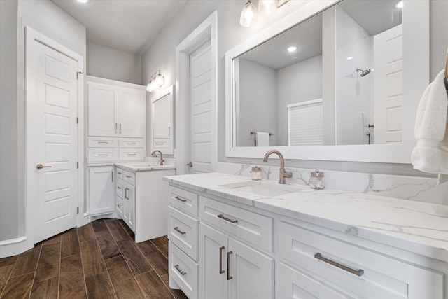 bathroom with tiled shower, two vanities, wood finish floors, and a sink