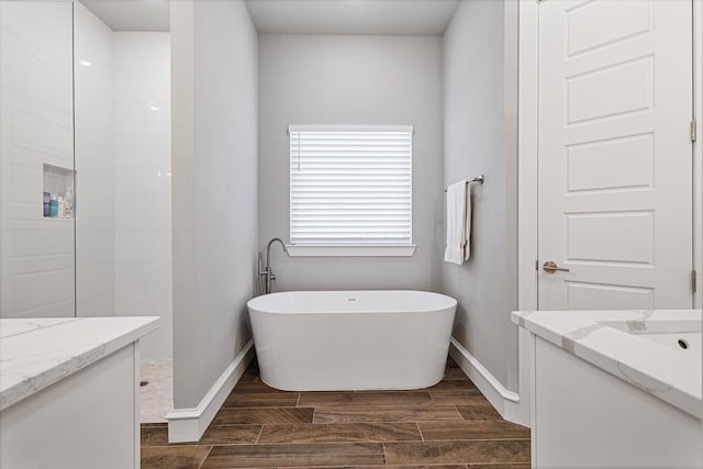 full bath featuring a walk in shower, baseboards, wood finish floors, a soaking tub, and vanity