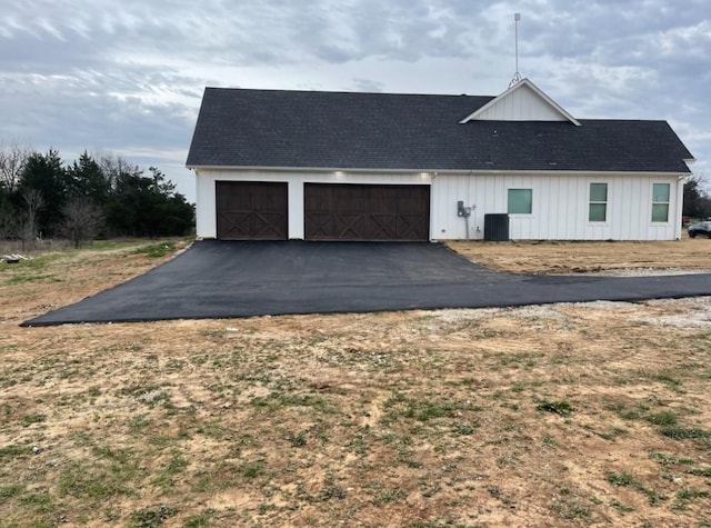 view of front facade featuring aphalt driveway, an attached garage, central AC unit, and board and batten siding