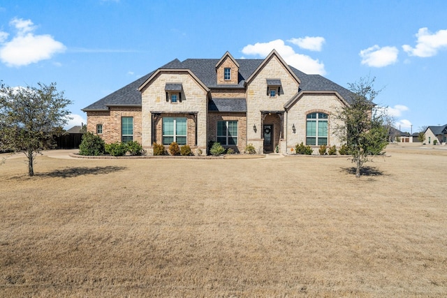 french provincial home with a shingled roof, stone siding, brick siding, and a front lawn