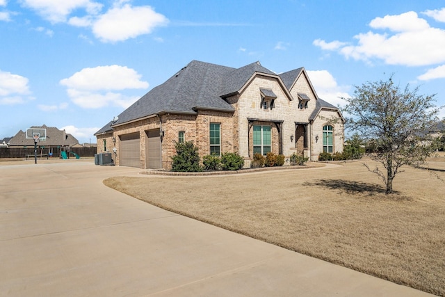 french country style house featuring a garage, a shingled roof, concrete driveway, stone siding, and brick siding