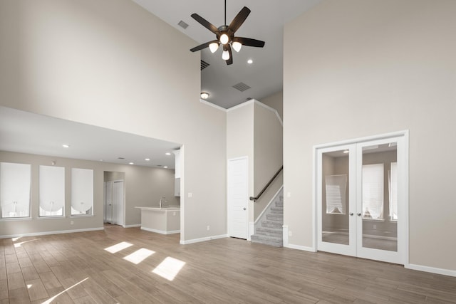 unfurnished living room with high vaulted ceiling, light wood-style flooring, a sink, baseboards, and french doors