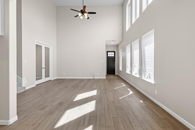 unfurnished living room featuring stairway, baseboards, wood finished floors, and french doors