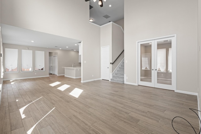 unfurnished living room with baseboards, stairway, a high ceiling, french doors, and light wood-type flooring